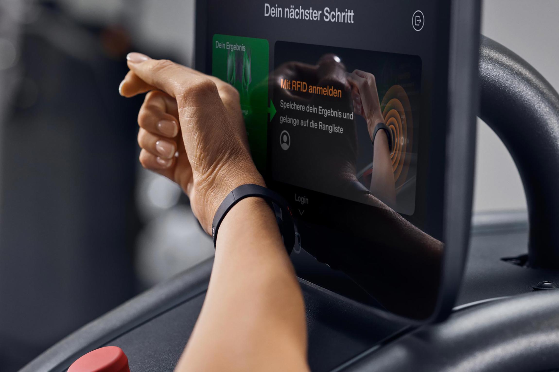 Eine Hand mit einem schwarzen Fitnessarmband interagiert mit einem digitalen Bildschirm auf einem Fitnessgerät. Der Bildschirm zeigt Anweisungen zur Anmeldung mittels RFID sowie Ergebnisse des Trainings. Die Atmosphäre wirkt modern und technikorientiert.
