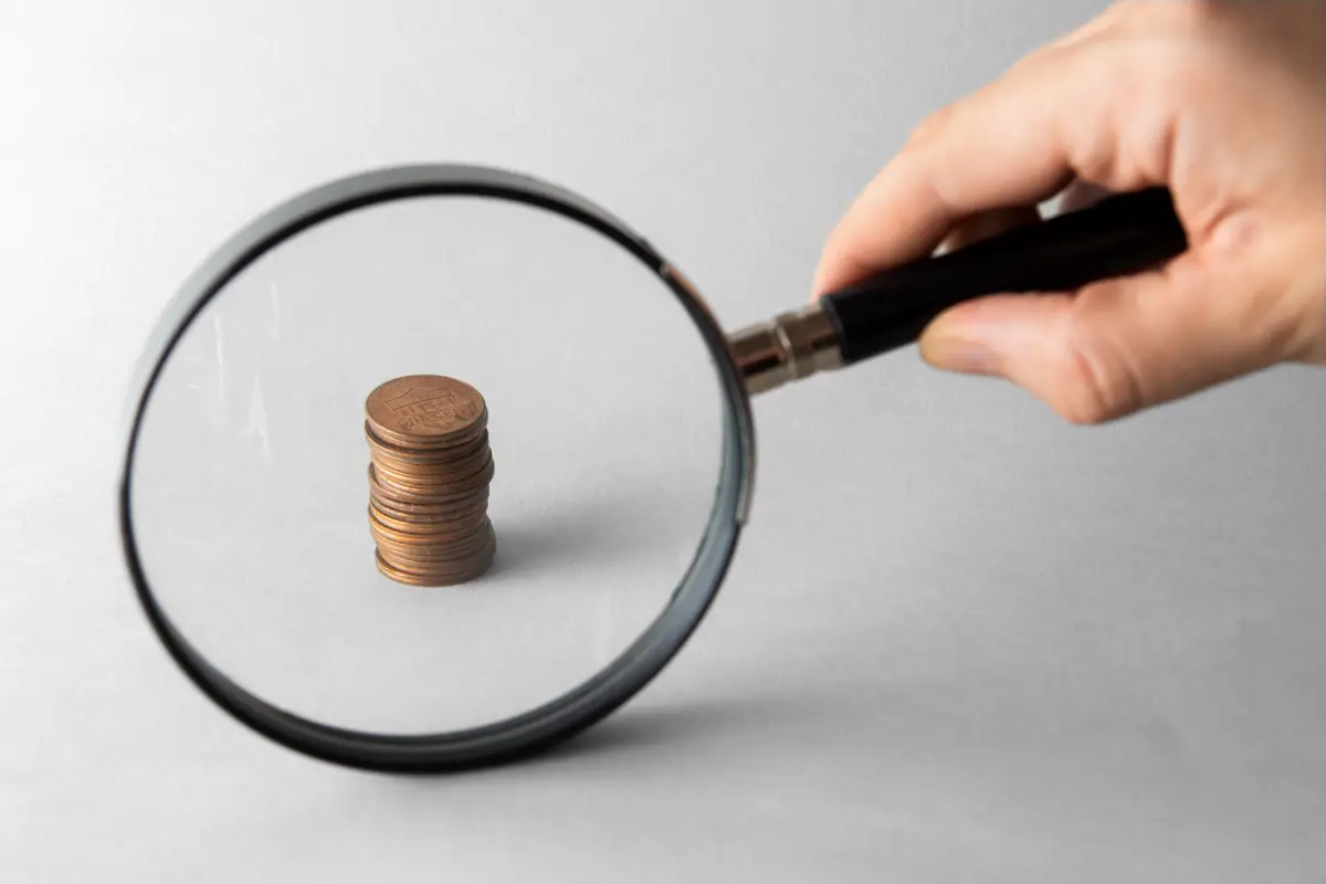 Stapel von Münzen, die durch eine Lupe betrachtet werden, symbolisiert die genaue Analyse von finanziellen Details.