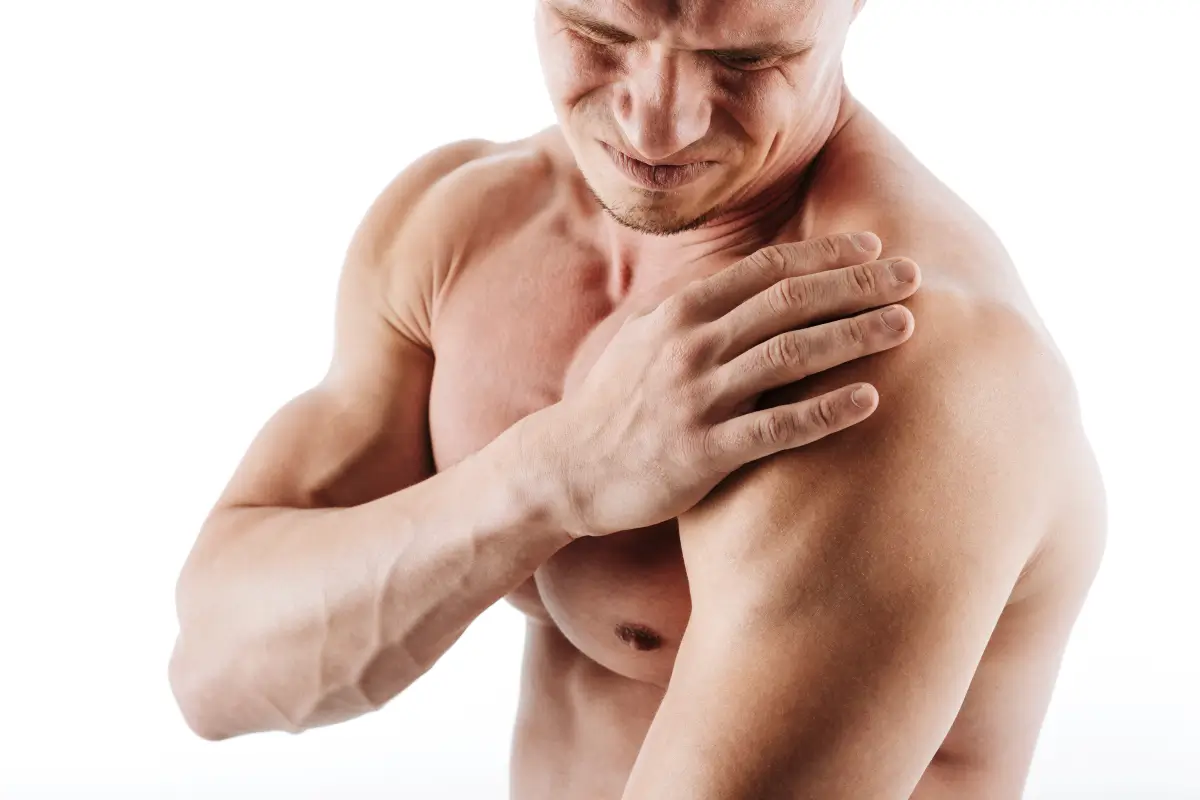 Nahaufnahme eines sportlichen Mannes mit nacktem Oberkörper, der sich mit schmerzverzerrtem Gesicht die schmerzende rechte Schulter hält.