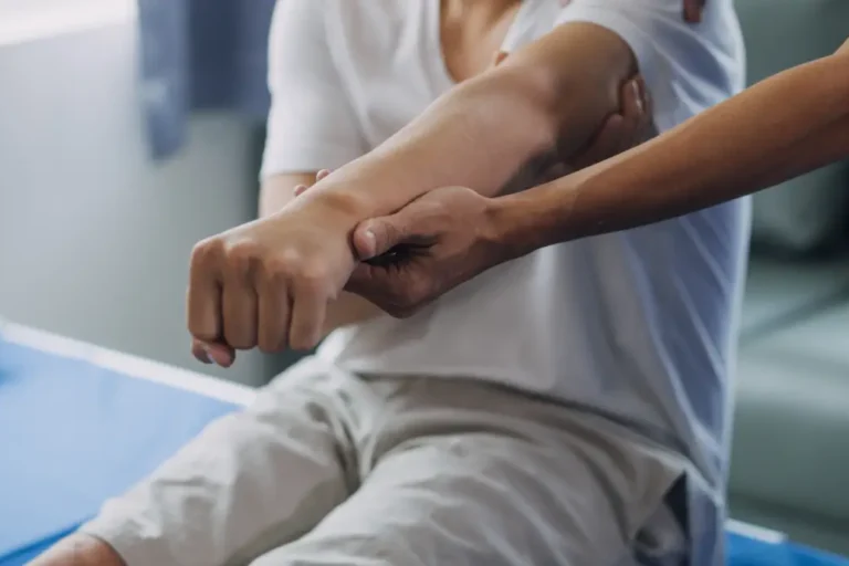Ein Patient führt unter der Anleitung eines Physiotherapeuten eine Übung zur Mobilisation des Arms durch. Die Hand des Physiotherapeuten stützt den Arm des Patienten, um die Bewegung zu kontrollieren.
