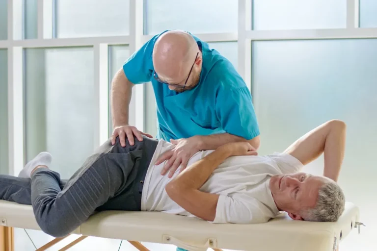 Physiotherapeut behandelt einen erwachsenen Mann auf einer Liege in einer modernen Klinik.
