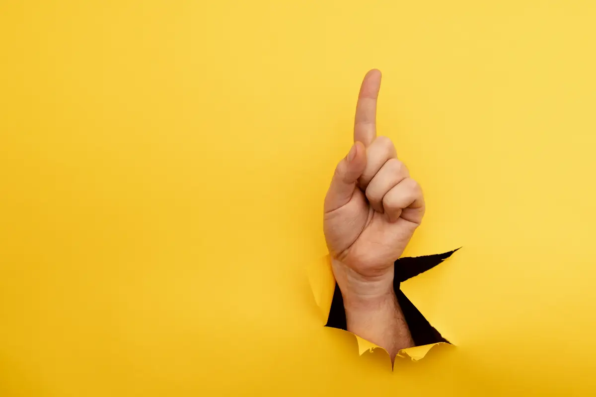 Hand mit ausgestrecktem Zeigefinger, der nach oben zeigt, vor einem leuchtend gelben Hintergrund, symbolisiert Richtung oder Hinweis.