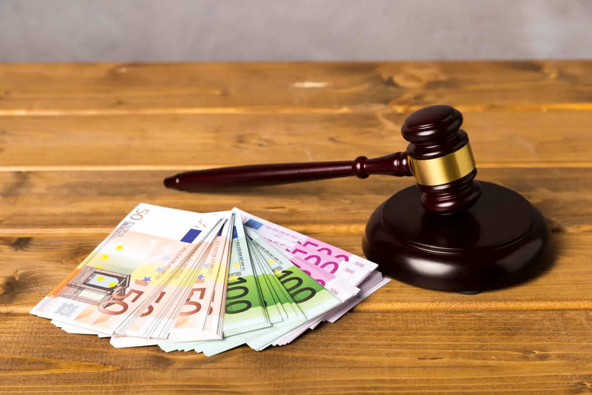 Ein Richterhammer aus Holz liegt neben einem Stapel Euro-Banknoten auf einem Holztisch, symbolisiert Rechtsangelegenheiten und finanzielle Entscheidungen.
