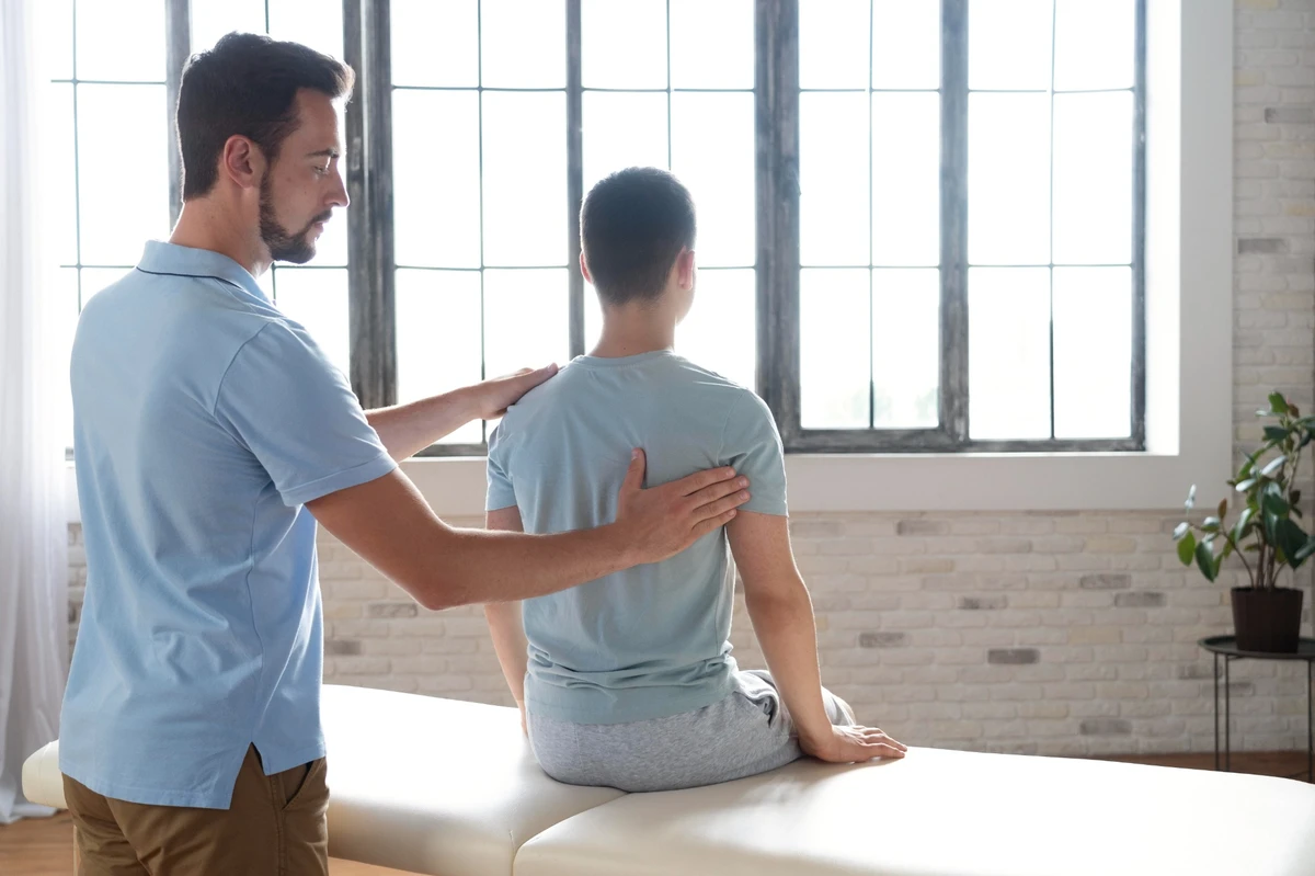 Physiotherapeut überprüft die Haltung eines sitzenden Patienten, um eine physiotherapeutische Behandlung vorzubereiten.