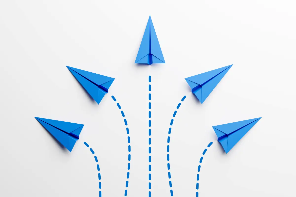 Fünf blaue Papierflieger, die verschiedene Wege einschlagen, symbolisieren Entscheidungsfindung und Alternativen.