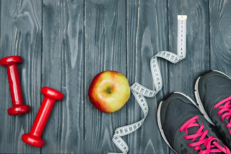 in roter Apfel, ein Maßband, Hanteln und Laufschuhe liegen auf einem dunklen Holzhintergrund, repräsentieren einen gesunden Lebensstil, Fitness und Gewichtsmanagement.