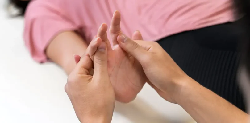 Nahaufnahme einer physiotherapeutischen Handbehandlung – Therapeut massiert die Handfläche einer liegenden Person zur Förderung der Beweglichkeit und Schmerzlinderung.