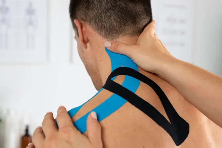 Physiotherapeutin bringt elastisches Kinesio-Tape auf den Nacken und die Schulter eines männlichen Patienten auf, um Verspannungen zu lindern und die Muskulatur zu unterstützen.
