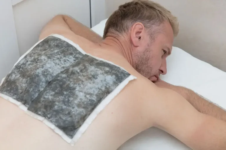 Ein Mann liegt entspannt auf einer Liege und erhält eine Fangopackung auf seinem Rücken während einer physiotherapeutischen Behandlung.