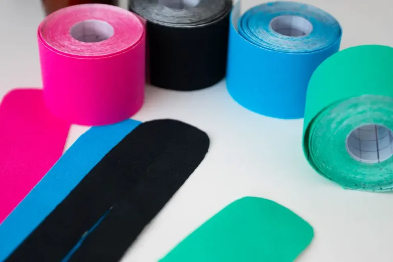Mehrere bunte Kinesio-Tape-Rollen in Pink, Schwarz, Blau und Grün mit zugeschnittenen Tape-Streifen, die für physiotherapeutische Anwendungen und Rehabilitation genutzt werden.