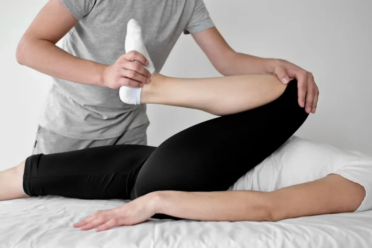 Physiotherapeut führt eine mobilisierende Beinübung bei einer Patientin in Seitenlage durch.