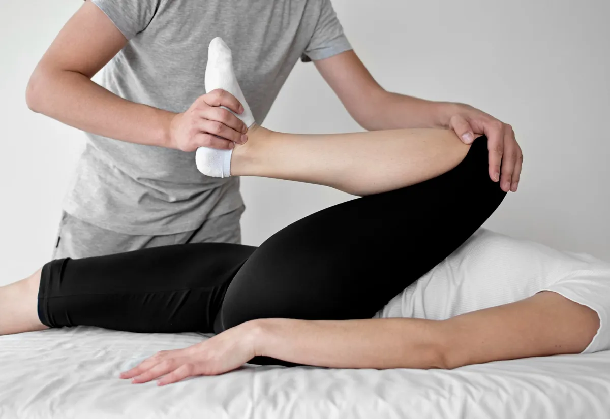 Physiotherapeut führt eine mobilisierende Beinübung bei einer Patientin in Seitenlage durch.