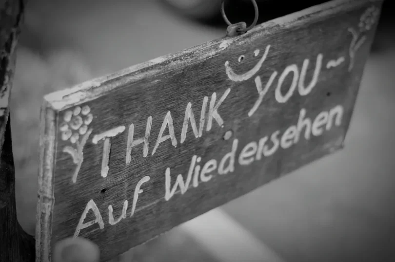Holzschild mit handgeschriebener Aufschrift 'Thank You – Auf Wiedersehen' und lächelndem Gesicht