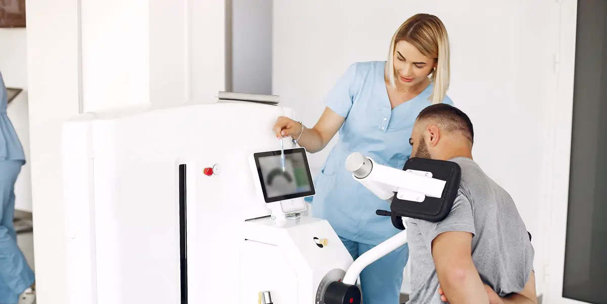 Physiotherapeutin betreut einen Patienten beim Training an einem Reha-Gerät in einer modernen Physiotherapiepraxis.