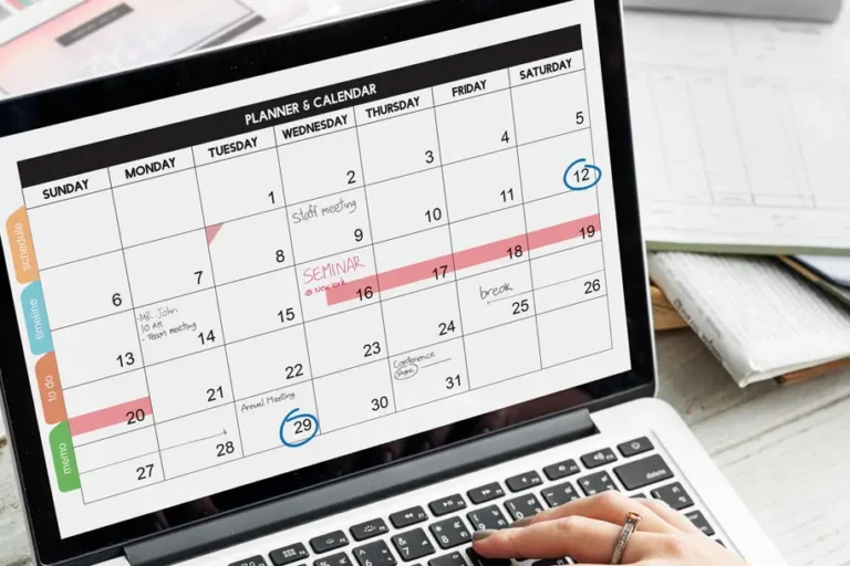 Person betrachtet einen digitalen Monatskalender auf einem Laptop, auf dem verschiedene Termine wie Meetings, Seminare und Pausen markiert sind.