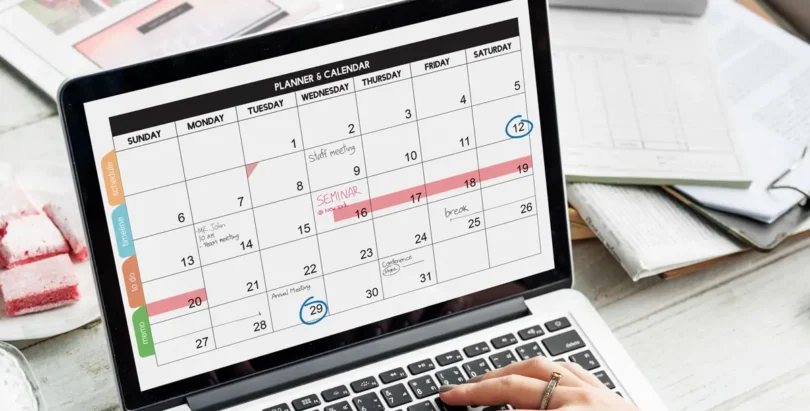 Person betrachtet einen digitalen Monatskalender auf einem Laptop, auf dem verschiedene Termine wie Meetings, Seminare und Pausen markiert sind.