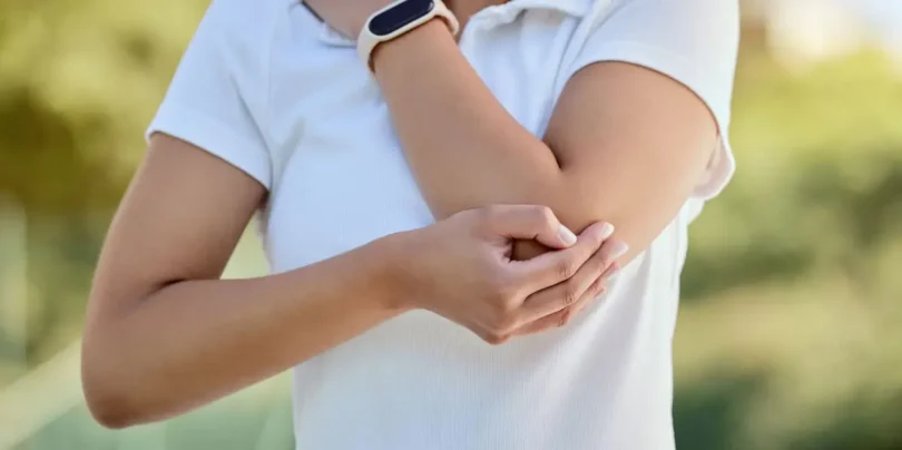 Frau mit Schmerzen im Ellenbogen hält sich den Arm – Symbolbild für Tennisarm und Ellenbogenbeschwerden