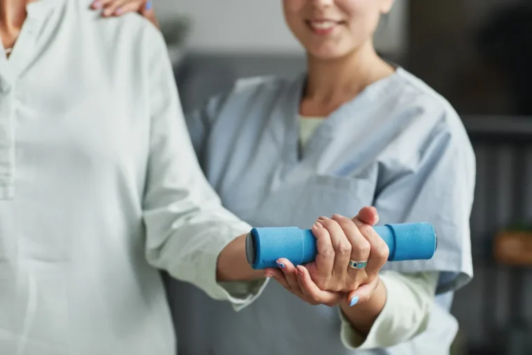 Seniorin trainiert mit Unterstützung durch eine Pflegekraft mit einer kleinen Hantel im Altersheim.