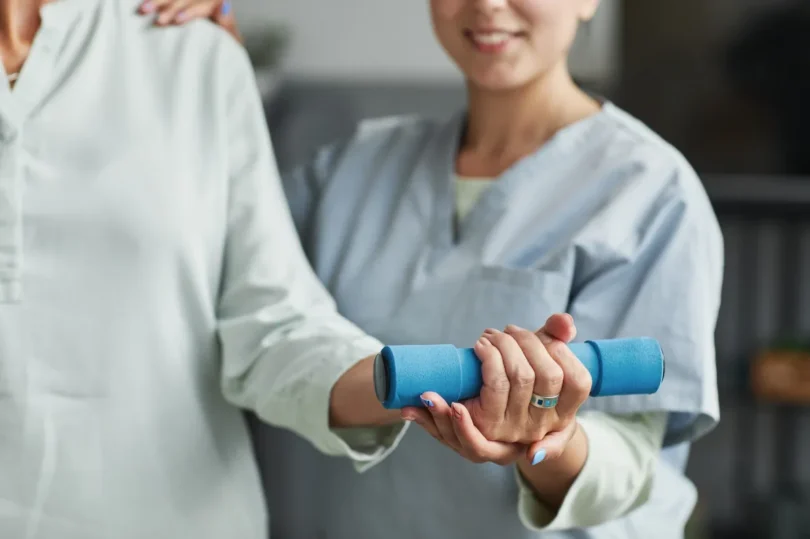 Seniorin trainiert mit Unterstützung durch eine Pflegekraft mit einer kleinen Hantel im Altersheim.