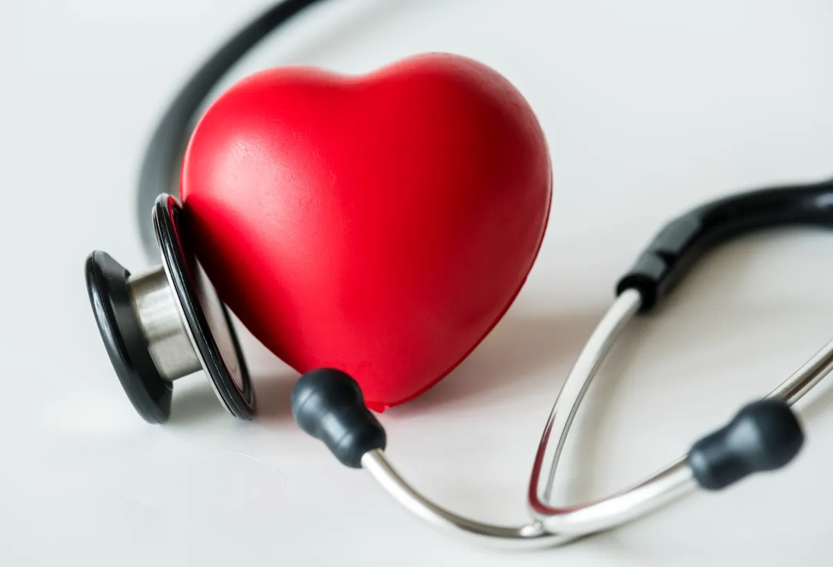 Ein rotes Herzsymbol liegt neben einem Stethoskop auf weißem Hintergrund – Symbol für Herzgesundheit und medizinische Vorsorge.