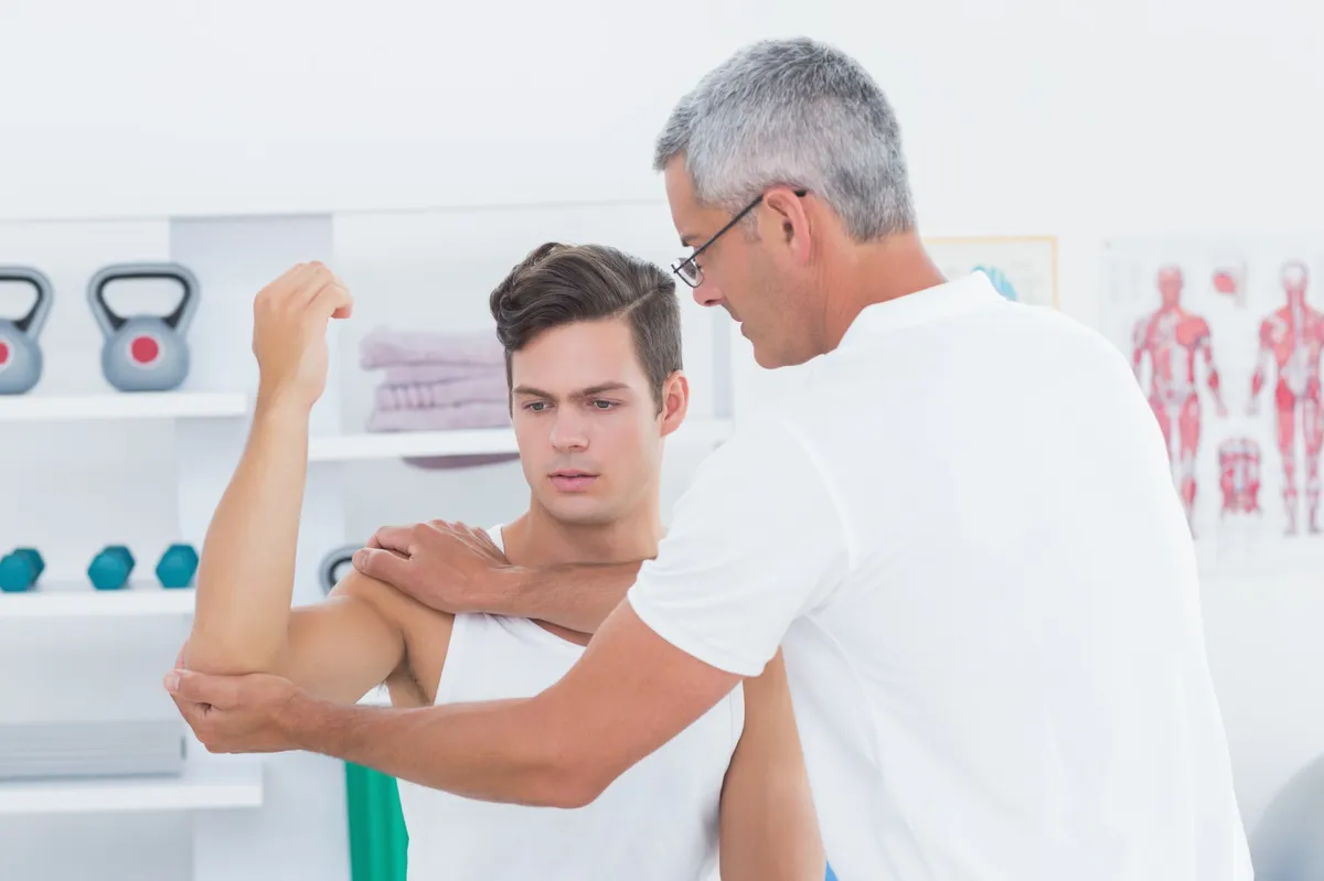 Therapeut dehnt den Arm eines jungen Patienten – physiotherapeutische Behandlung zur Mobilisierung der Schulter.